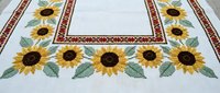 Handmade cross stitch tablecloth with bright sunflowers and red geometric border on white linen fabric, traditional folk embroidery craft.