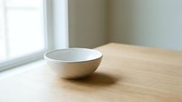 Empty white ceramic bowl on wooden table near window with natural light for kitchen dining and home decor concepts.