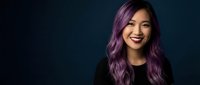Young Asian woman with vibrant purple hair smiling confidently against dark background. Modern portrait for beauty, fashion and lifestyle concepts.