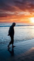 Elderly Caucasian man walking barefoot along ocean shore at vibrant sunset, reflecting solitude, retirement, and peaceful aging by the sea.