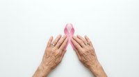 Elderly hands protecting pink breast cancer awareness ribbon on white background symbolizing support, hope and healthcare advocacy for women's health.
