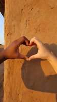 Diverse hands forming heart shape against warm adobe wall with shadow, symbolizing unity, love and multicultural friendship in golden sunlight.