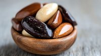 Mixed nuts in wooden bowl with dark and light colored almonds, brazil nuts, and pecans on rustic surface, macro food photography.
