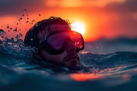 Male swimmer in goggles emerges from ocean water during dramatic sunset, with water droplets splashing around face against vibrant orange sky and glowing sun.