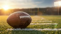 American football on grass field with stadium lights and golden sunset creating dramatic sports atmosphere for game day.