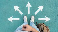 Young person standing at crossroads with white directional arrows on turquoise pavement, symbolizing life choices and decision-making process.