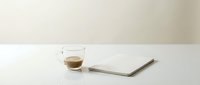 Espresso cup with saucer and notebook on white surface for coffee break, workspace, and beverage concepts.