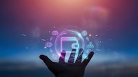 Hand holding glowing digital technology icons with computer and network symbols floating above palm against purple gradient background.