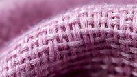 Extreme close up of pink knitted fabric texture showing detailed wool or cotton fibers in macro photography. Soft focus background creates dreamy atmosphere.