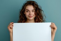 Young woman with curly brown hair holding blank white poster against turquoise background, perfect for advertising, announcement or promotional content display.