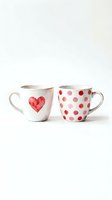 Pair of ceramic mugs with watercolor heart and polka dot designs in red and pink tones, isolated on white background, ready for product mockups and merchandise design.