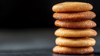 Stack of golden brown macarons or cookies with sparkly sugar coating against dark background, macro food photography with selective focus and bokeh effect.