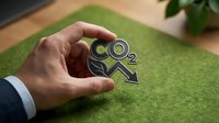 Businessman hand protecting CO2 carbon dioxide emission symbol on green moss surface representing environmental responsibility and climate action.