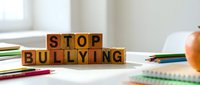 Wooden letter blocks spelling Stop Bullying on a school desk with colorful pencils and an apple, raising awareness against harassment in education.