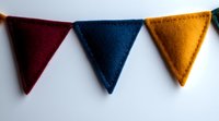 Colorful felt triangle bunting featuring burgundy, navy blue and mustard yellow pennants against white background, suitable for party decoration and festive design elements.