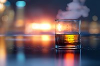 Glass of whiskey on reflective surface with warm glowing bokeh background and dramatic lighting creates moody atmosphere for beverage photography.