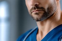 Close-up portrait of a bearded male healthcare professional wearing blue scrubs in a clinical setting, suitable for medical and wellness content.