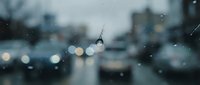 Cracked windshield with spider web damage on blurred city street background with bokeh lights and raindrops during evening traffic for insurance concepts.