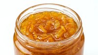 Homemade apricot jam in glass jar with wooden spoon, preserved fruit spread for breakfast, baking, and culinary use.