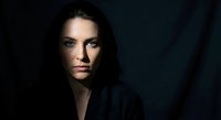 Professional portrait of confident young Caucasian businesswoman with dark hair against dramatic black background for corporate branding and marketing.
