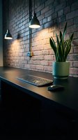 Modern industrial workspace with pendant lights illuminating brick wall, featuring computer keyboard and snake plant on dark wooden desk for office design.