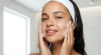 Young Hispanic woman applying facial cleanser in modern bathroom during morning skincare routine for healthy glowing skin and self-care wellness.