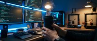 Professional software developer programming at modern workstation with multiple monitors displaying code in dark office environment at night.