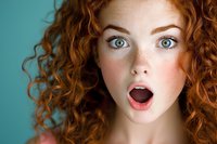 Young woman with natural red curly hair and surprised facial expression against turquoise background, showing genuine emotion and amazement.