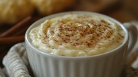 Creamy rice pudding topped with cinnamon in white ceramic bowl, close-up view showing rich texture and swirled spice garnish against rustic background.