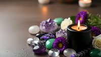 Spa wellness setup with healing crystals, purple flowers, candle and gemstones for meditation and relaxation therapy on dark surface.