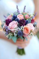 Romantic wedding bouquet with pink roses, blue thistle, purple allium, and delicate white flowers against soft blurred background, fresh floral arrangement for bride.
