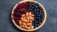 Fresh blueberries, dried cranberries and raw almonds arranged in wooden bowl on dark background, healthy snack mix of antioxidant superfoods.
