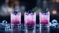 Purple sparkling cocktails garnished with fresh blueberries and rosemary sprigs in crystal glasses on dark background with ice cubes and bokeh lights.