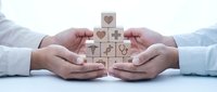 Hands protecting wooden blocks with healthcare symbols including medical cross and hearts representing health insurance and medical care protection.