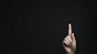 Hand with raised index finger emerging from darkness against black background, dramatic lighting creates mysterious minimalist composition for attention-grabbing designs.