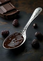 Silver spoon with melted chocolate, dark chocolate pieces and fresh blackberries on rustic black background, gourmet dessert preparation.