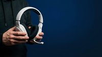 White wireless headphones held by male hands against dark blue background, suitable for audio equipment marketing and technology promotions.