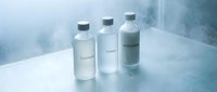 Three minimalist glass bottles with silver caps containing skincare products arranged on white surface with soft natural lighting and clean aesthetic.