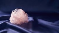 Translucent crystalline mineral specimen resting on dark blue silk fabric, showcasing natural geometric formations and light refraction for geology and science education.