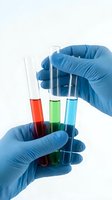 Laboratory technician wearing blue nitrile gloves holding test tubes with red, green, and blue chemical solutions for scientific research and medical testing.