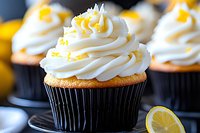 Fresh lemon cupcake topped with swirled vanilla buttercream frosting and yellow zest garnish on dark background, selective focus on center dessert.