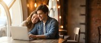 Young couple working together on laptop in cozy cafe with warm lighting and brick walls, sharing intimate moment while browsing online content.