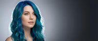 Young woman with vibrant turquoise blue wavy hair on gradient background for beauty salon advertising and hair color transformation concepts.