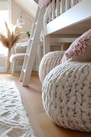 Cozy scandinavian interior with chunky knit pouf, pampas grass, and white ladder in modern bedroom. Soft beige and white color scheme creates calm atmosphere.