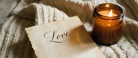 Cozy romantic scene with a glowing amber candle and a handwritten love note on aged paper, set on a soft knit sweater background.