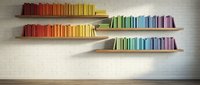 Colorful books arranged by rainbow spectrum on modern floating wooden shelves against white brick wall creating organized library display for interior design.