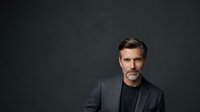 Middle-aged Caucasian male professional wearing charcoal blazer and black shirt against dark studio background. Corporate headshot suitable for business profiles, websites, and professional portfolios.