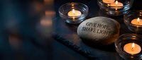 Inspirational stone with give hope share light message surrounded by glowing candles creating warm peaceful atmosphere for meditation and spiritual reflection.