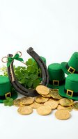 Horseshoe with lucky coins, clover leaves and green leprechaun hats arranged on white background for St. Patrick's Day celebrations and festive designs.