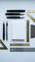Flat lay of professional drafting tools including fountain pens, rulers, protractor and blank notebook on white background for design and architecture work.